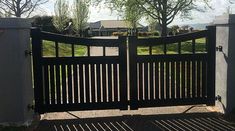 a black gate in front of a house with trees and grass on the other side