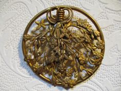 a gold brooch that is sitting on a white tablecloth with an intricate design in the center