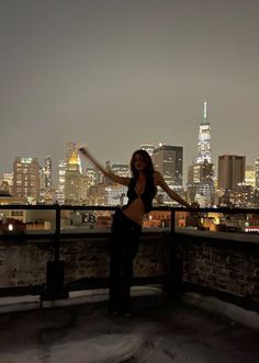 a woman standing on top of a roof in front of a city skyline at night