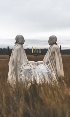 two people sitting in the middle of a field with three candles on each side of them