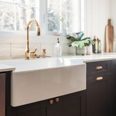 a white kitchen sink sitting under a window next to a wooden counter top with brass faucet