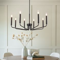 a chandelier hanging over a dining room table with flowers in the vase on it