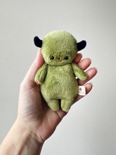 a hand holding a small green stuffed animal with horns on it's head and eyes