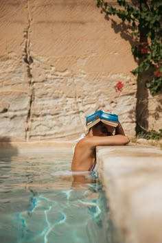 a woman is sitting in the water wearing a hat and reading a book on her head