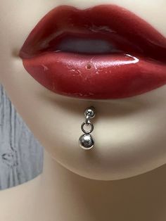 a mannequin's face with red lipstick and silver earrings on its nose