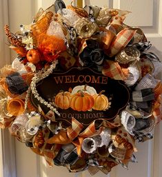 a welcome to our home wreath with pumpkins and ribbons hanging on the front door