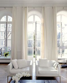 a living room filled with white furniture and large windows