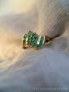 an emerald and diamond ring sitting on top of a white cloth