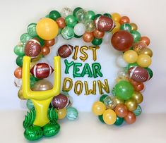 a balloon wreath with footballs, balloons and streamers around it that says 1st year down