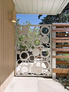 an open gate on the side of a house with wooden slats and metal circles