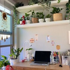 a laptop computer sitting on top of a wooden desk next to potted plants and other office supplies