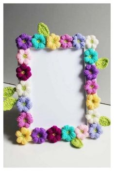 a crocheted photo frame with colorful flowers on the front and bottom, sitting on a white surface