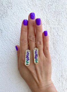 a woman's hand with purple and green nail polish holding two matching gold earrings