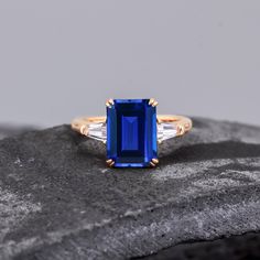 an emerald and diamond ring sitting on top of a rock with two baguettes