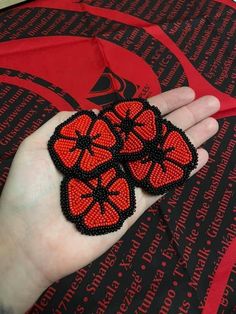 a hand holding three red and black beaded flowers