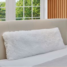 a white fluffy pillow sitting on top of a bed next to a pair of windows