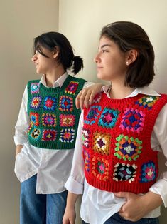 two women standing next to each other in front of a wall wearing colorful sweaters