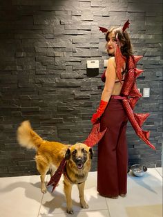 a woman standing next to a dog in front of a brick wall wearing red gloves