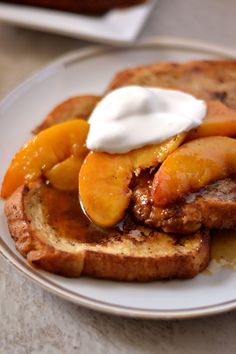 a plate topped with french toast covered in peaches and whipped cream on top of it