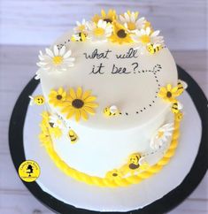 a white cake with yellow flowers and bees on it that says, what will it be?