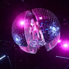 a person standing on top of a disco ball in the air with lights behind them