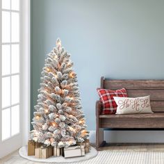 a small christmas tree in front of a bench with presents on it and a pillow