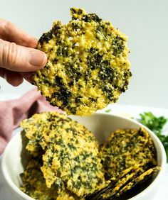 a person is holding up some food in a white bowl on a plate with parsley