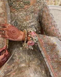 a woman with henna on her hands sitting in a chair wearing a dress and holding flowers