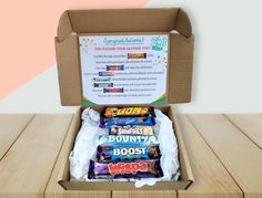 an open cardboard box filled with assorted candy bar's on top of a wooden table