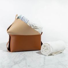 a tan leather bag with two white towels and a folded towel on the ground next to it