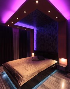 a large bed sitting under a purple light in a bedroom