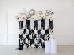 a black and white backdrop with balloons, streamers and other decorations on the wall