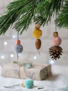 three ornaments hanging from a christmas tree next to a wrapped present box and pine cone