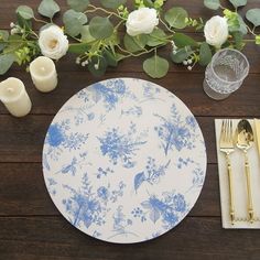 a place setting with blue and white plates, silverware and flowers on a wooden table