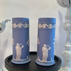 two blue vases sitting on top of a black table next to a white wall