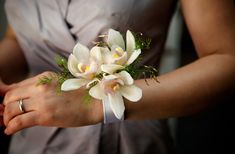 a woman wearing a ring holding a bouquet of white flowers in her hands with greenery on the wrist