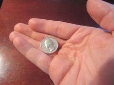 a person holding a coin in their left hand on top of a wooden table,