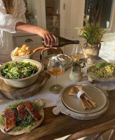 a woman pouring wine into a bowl on top of a table filled with plates and bowls