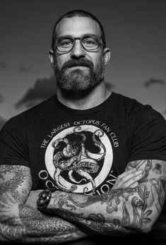 a man with tattoos and glasses is looking at the camera