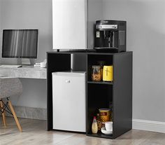 a small refrigerator next to a desk with a computer monitor and coffee maker on it