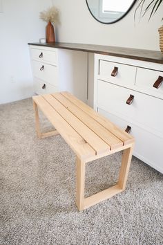 a wooden bench sitting on top of a carpeted floor next to a white dresser