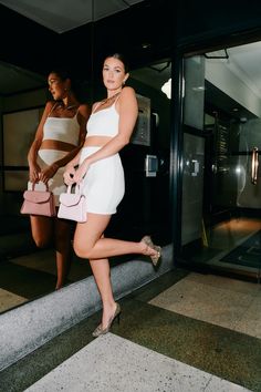 two women in white dresses are walking down the street with purses on their feet