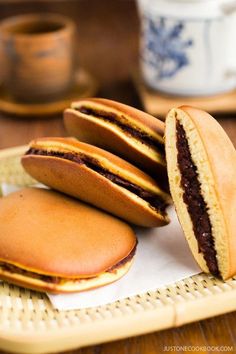 three cookies sitting on top of each other in front of two cups and saucers