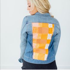 a woman wearing a jean jacket with an orange and white patchwork design on the back