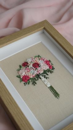 a cross stitch bouquet in a wooden frame on a pink fabric covered bedding area