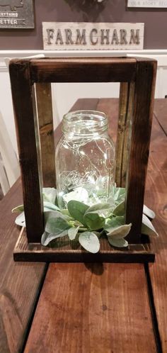 a wooden frame with a glass jar filled with water and greenery sitting on top of a table