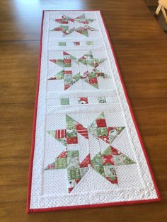 a quilted table runner with red and green stars on the top, sitting on a wooden floor