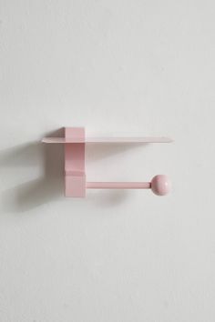 a pink wall mounted shelf next to a white wall with an object on it's side