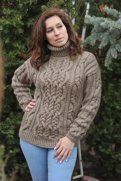 a woman standing in front of a tree wearing a sweater and jeans with her hands on her hips