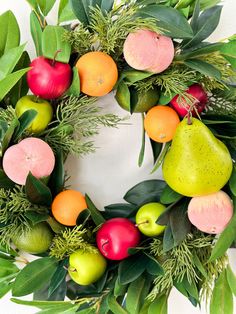 a wreath with apples, pears, oranges and green leaves on white background